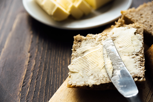 A knife spreading butter on bread on wooden background