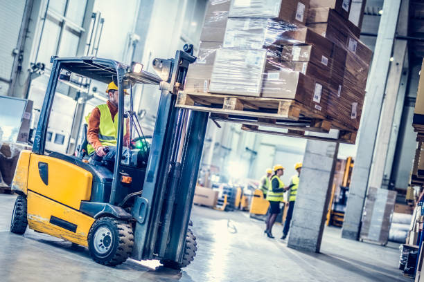 Forklift moving stack of boxes Forklift in foreground moving stack of boxes, warehouse workers in background. forklift photos stock pictures, royalty-free photos & images