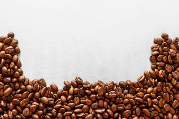 Coffee beans are scattered by a close up on a white table, top view, there is a place for the text