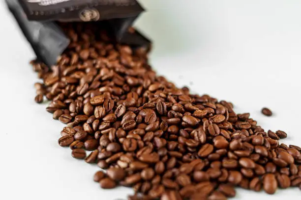 Coffee beans scattered on a table from a package blurred background with selective focus