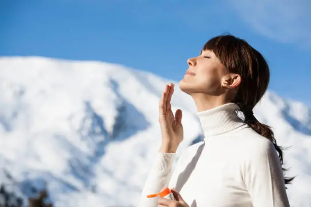 Photo of woman in the snowy mountains applying cream on her face