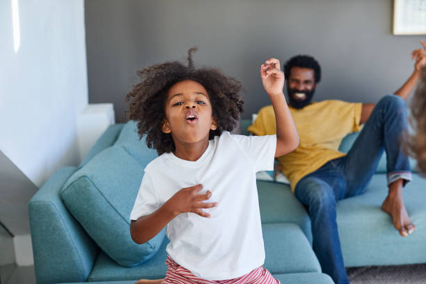 That's my boy, the little rocker! Shot of a cheerful young father and his son dancing on a couch while listening to music at home during the day air guitar stock pictures, royalty-free photos & images