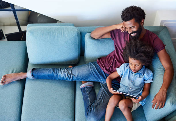 Mom better not catch us relaxing like this High angle shot of a carefree young father and son browsing on a digital tablet while relaxing on a couch at home during the day child candid indoors lifestyles stock pictures, royalty-free photos & images