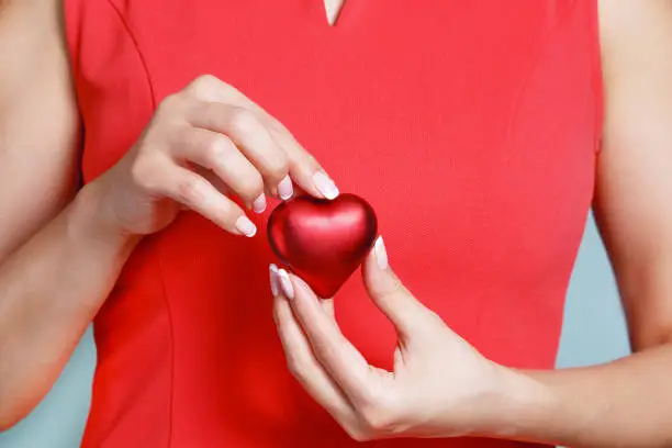 Valentine's day symbol - red heart in the hands of a woman on a turquoise background.