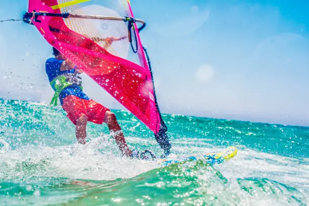 Side view of a windsurfer riding on turquoise water on a sunny day.