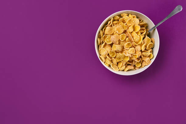 istock Bowl with corn flakes and spoon on purple background, top view 910017238