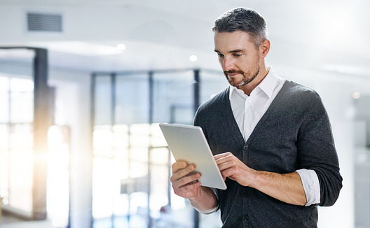 Cropped shot of a handsome mature businessman using his digital tablet while standing in the office