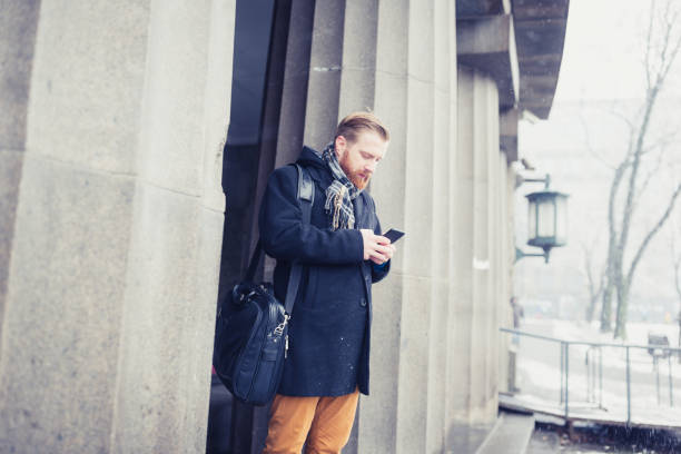 istock Ginger businessman standing on office building entrance, using mobile phone. Snow is falling, It's a cold winter time.  Belgrade, Serbia, Europe 910035770