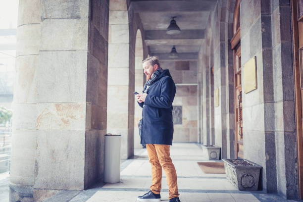 istock Young redhead businessman using mobile phone, on a office building entrance stairs 910038070