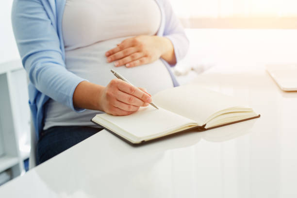 istock Pregnant woman writes to her diary on a white table 910049938