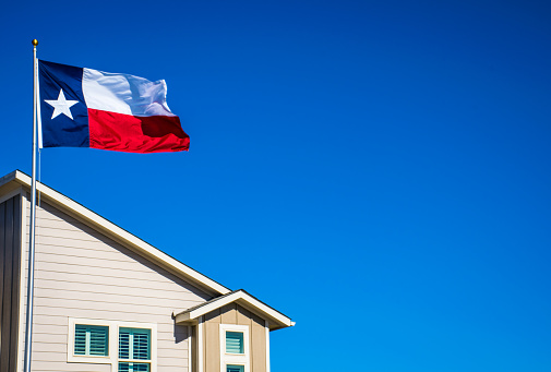 Texas State Flag the Symbol of the Lone Star State above Modern Brand New Suburban Home with blue sky and perfect sunny lighting