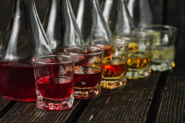 cordiali alcolisti assortiti in bicchieri e decanter su sfondo legno scuro - fruit liqueur foto e immagini stock
