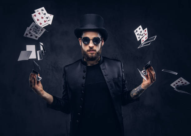 Magician showing trick with playing cards. Magician in a black suit, sunglasses and top hat, showing trick with playing cards on a dark background. magician stock pictures, royalty-free photos & images
