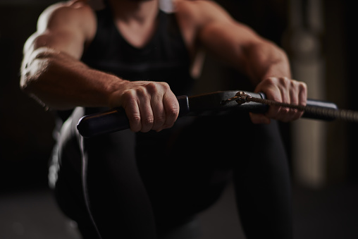 Unrecognized male athlete performing seated rowing exercise during cross training class in the gym.