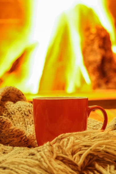 istock Orange mug for tea or coffee, wool things near cozy fireplace, winter vacations, selective focus. 910085778