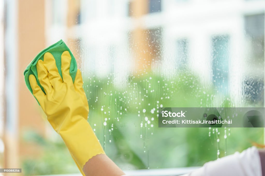 Woman housekeeper cleaning the mirror with green cloth. Cleaning Stock Photo