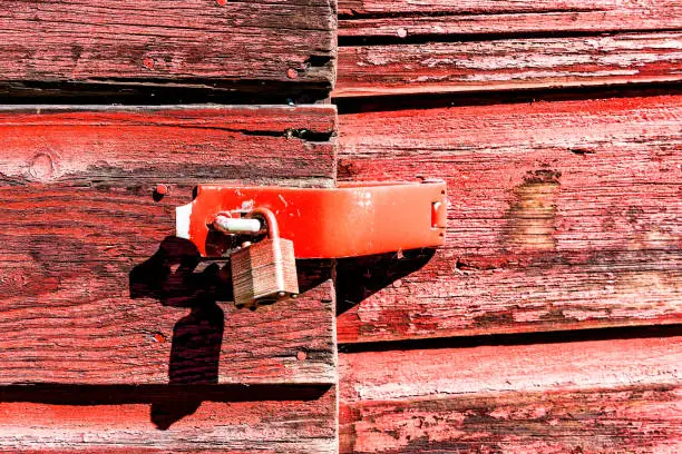 Macro closeup of retro vintage red wooden barn, shed exterior with locked doors and peeling old paint