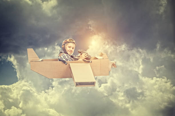 istock Low Angle Portrait Of Boy Flying Airplane Against Cloudy Sky 910090902