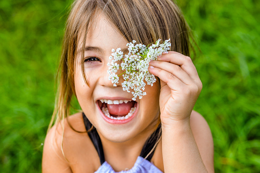 Adorable little child in a green field holds up a queen anne's lace flower to her eye and makes a fun, silly, happy face