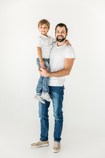 happy father holding adorable little son and smiling at camera isolated on white