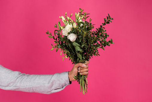 Cropped image of woman holding bouquet of flowers in hand isolated on pink