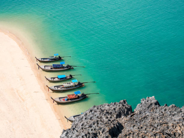 vista desde arriba de barcos de cola larga madera pequeña en la costa de una vacía playa de arena blanca y mar turquesa. montón de habitación y espacio para el texto de la copia. pequeña de la roca en primer plano. tailandia. - nautical vessel sky andaman sea beach fotografías e imágenes de stock