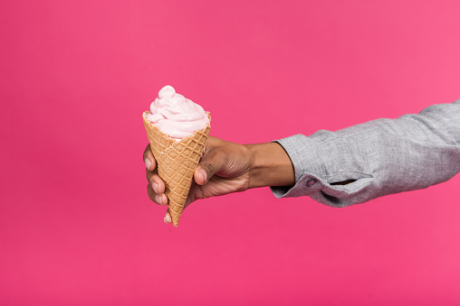 Cropped image of woman holding ice cream in her hand isolated on pink