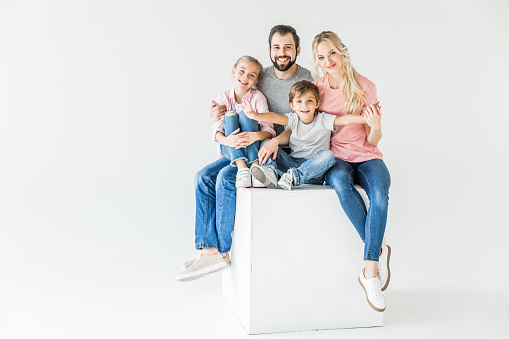 happy young family with two kids sitting together and smiling at camera isolated on white