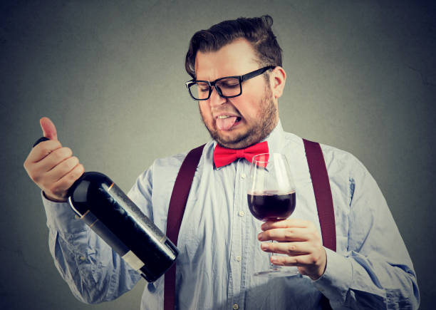 Man tasting wine and looking at bottle Man in bowtie trying wine and looking dissatisfied while exploring bottle. sour face stock pictures, royalty-free photos & images