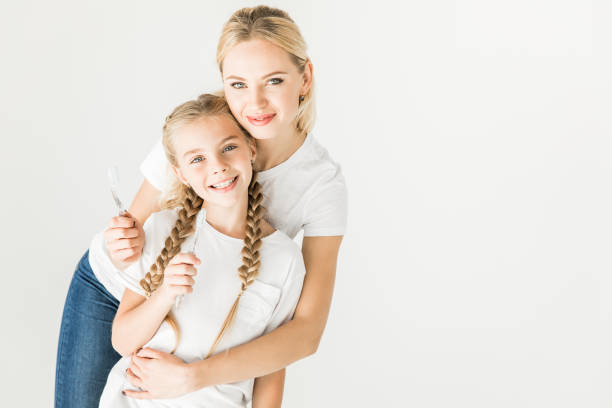 happy mother and daughter holding toothbrushes and smiling at camera isolated on white