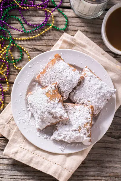 New Orleans traditional beignets with mardi gras beads on rustic wood table with chicory coffee, aerial view.