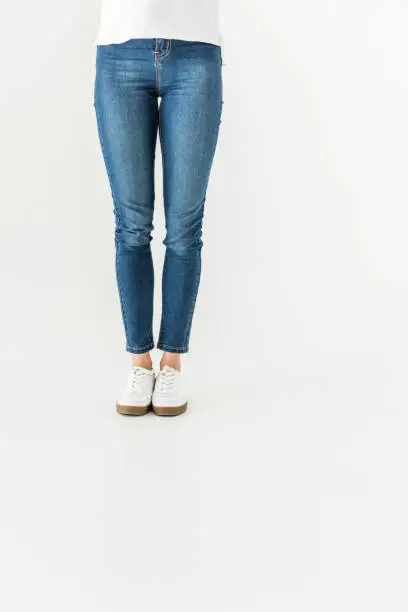 low section of young woman in denim pants and shoes standing isolated on white