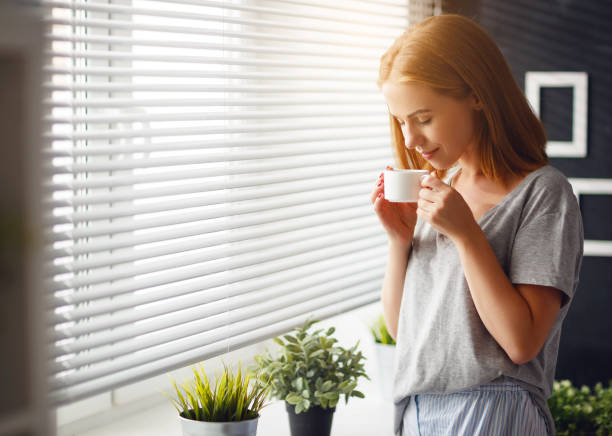felice giovane donna incontra la mattina con una tazza di caffè alla finestra - waking up window women morning foto e immagini stock