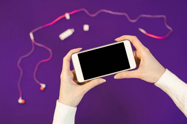 istock Woman hands white sweater using cellphone holding smart mobile phone with oled display on ultra violet color of year background accessories headphones. Close up Flat Lay bussines composition Top view trend 910169646