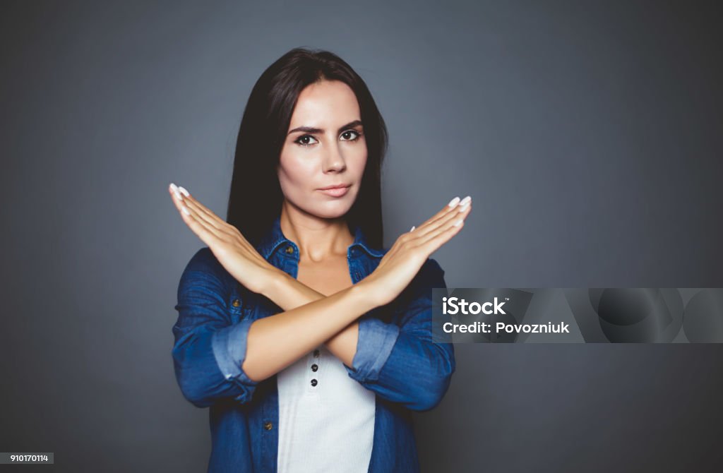 You can not. You can not. Young confident serious woman holding hands cross in front of the camera on a gray background isolated. Stop Gesture Stock Photo