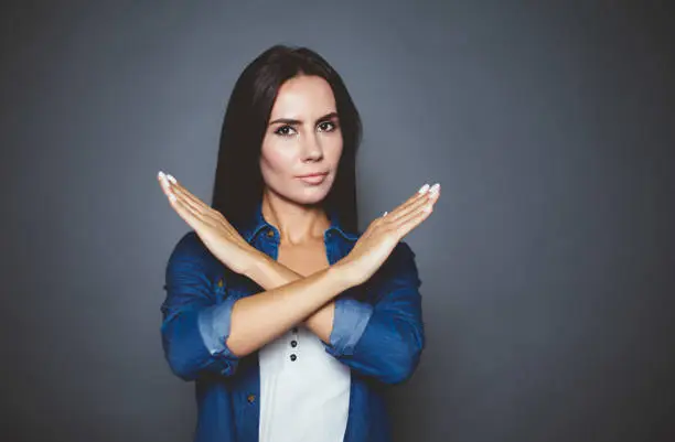 You can not. Young confident serious woman holding hands cross in front of the camera on a gray background isolated.