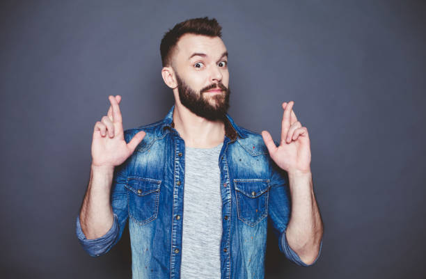 istock If only it would work. Young handsome man in jeans shirt with crossed fingers looking up against a gray background. Make a wish. 910170310