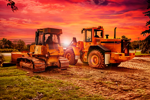 Large bulldozers at construction site, cloudy sky and sunset in background.