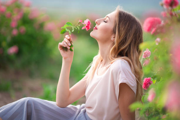 Beautiful young girl is wearing casual clothes having rest in a garden with pink blossom roses stock photo