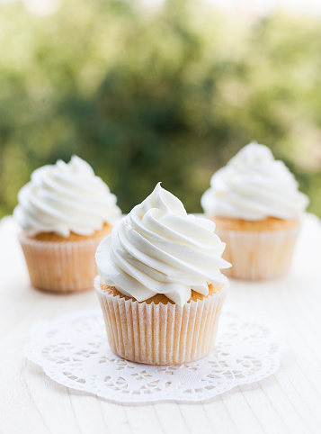 White vanilla cupcakes topped with swirl of sweet vanilla frosting captured on the table in a sunny day.