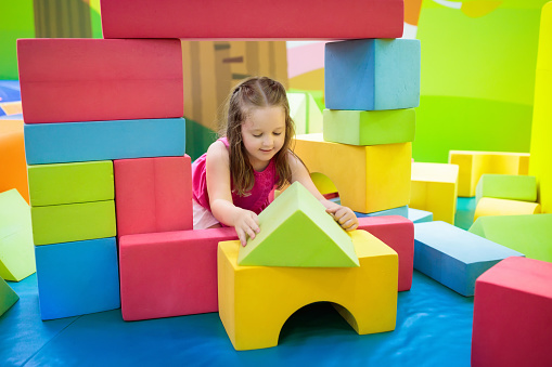 Child playing with colorful construction toy blocks. Educational toys for young kids. Kindergarten or preschool play room. Toddler kid at day care playground. Girl building house with block at daycare