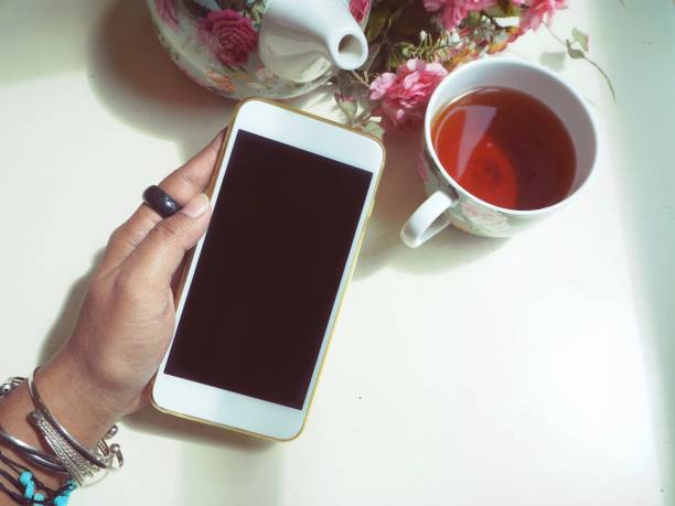 istock Woman using smart phone with tea pot and cup 910248932
