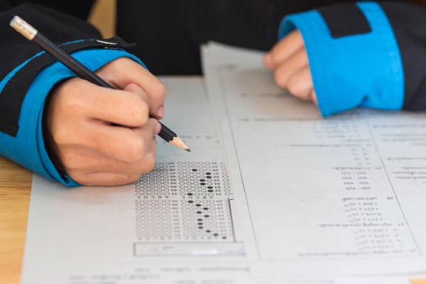 istock School Students hands taking exams, writing examination room with holding pencil on optical form of standardized test with answers and english paper sheet on desk doing final exam in classroom. 910255866