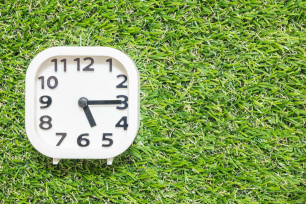 istock Closeup white clock for decorate show a quarter past five o'clock or 5:15 p.m. on green artificial grass floor textured background with copy space 910292936