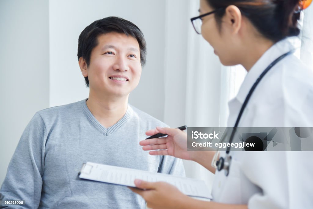 Female Doctor examining male patients. Asian Female Doctor examining and taking note on checklist paper with male patients in medical room. Patient Stock Photo