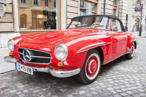 A red colored 1950s vintage Mercedes-Benz 190 SL roadster parked in downtown Ljubjana, Slovenia during a vintage car show.
