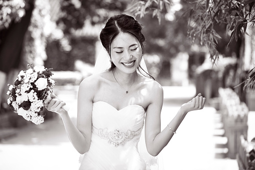 young and beautiful asian bride rejoicing with bouquet in hand, black and white.