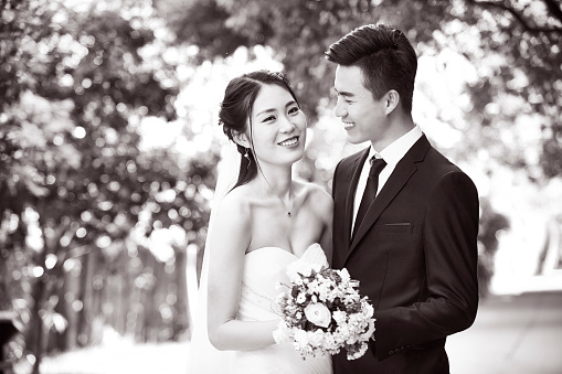 outdoor portrait of asian bride and groom looking at camera smiling, black and white.