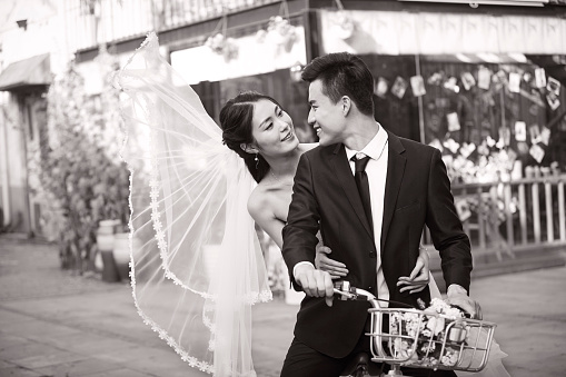 romantic asian newlywed couple having fun riding bicycle together in old market.