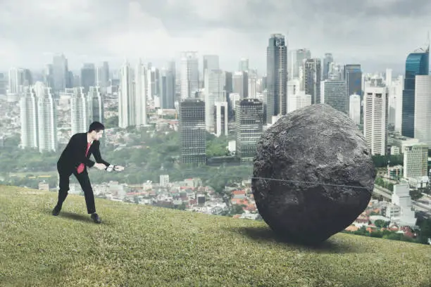 Arabian male manager pulling a stone while climbing on the hill with modern city background